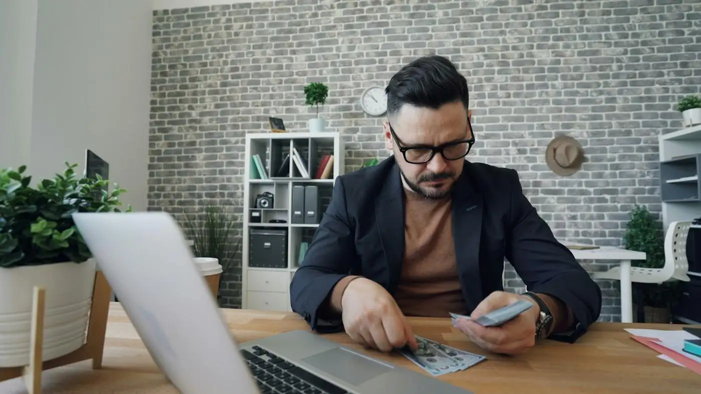 A business owner at a desk reviewing payments on a phone and laptop