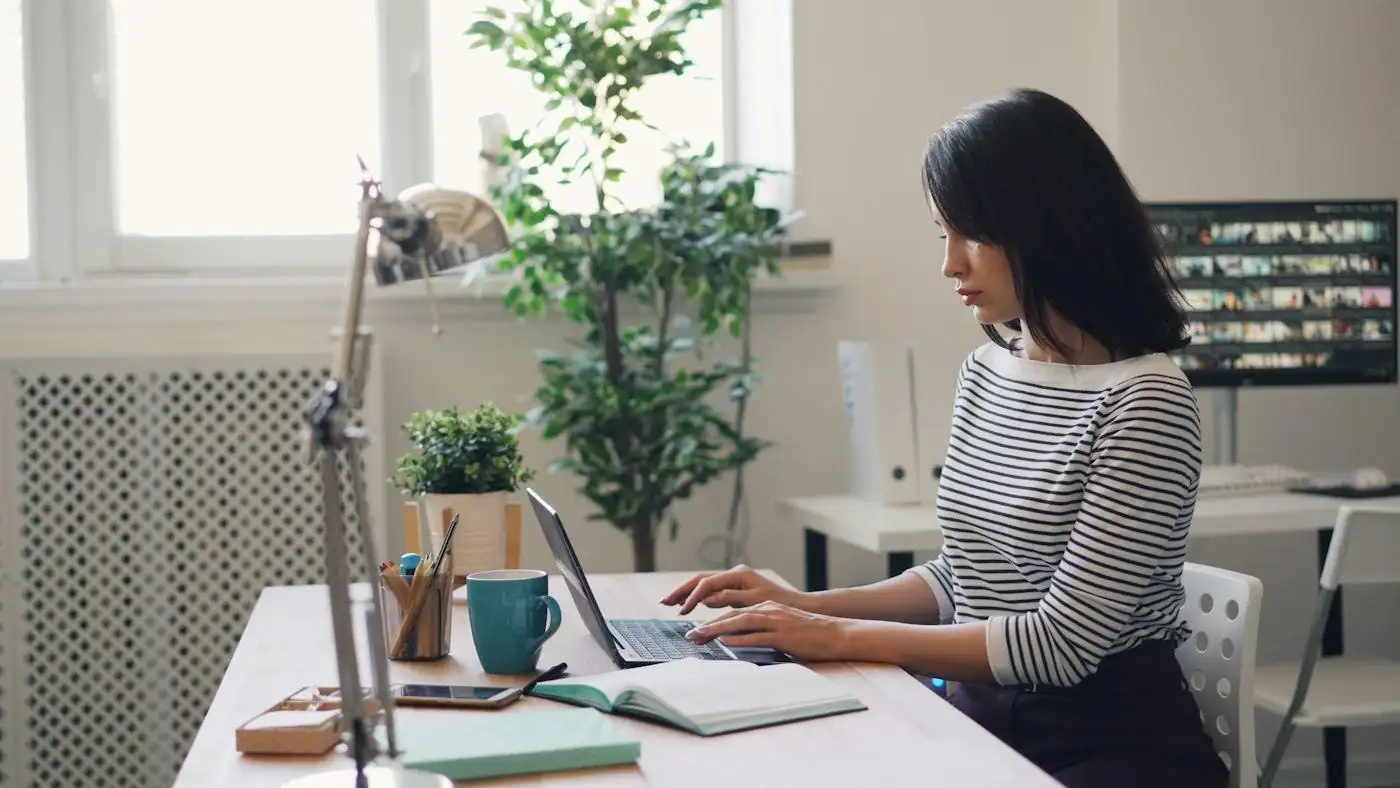 A person working through the books on a laptop at a bright desk