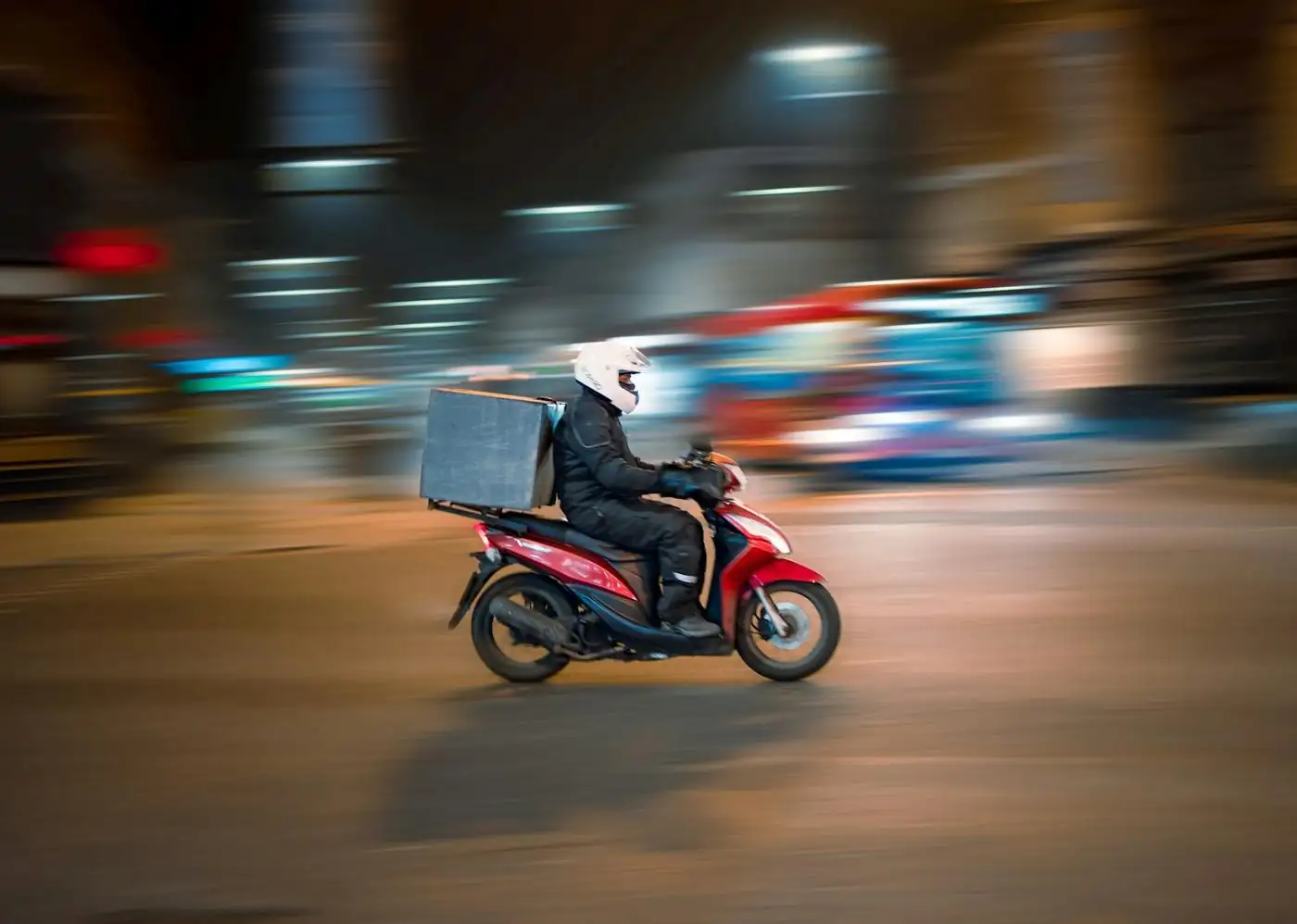 A courier on a scooter moving through city traffic at night