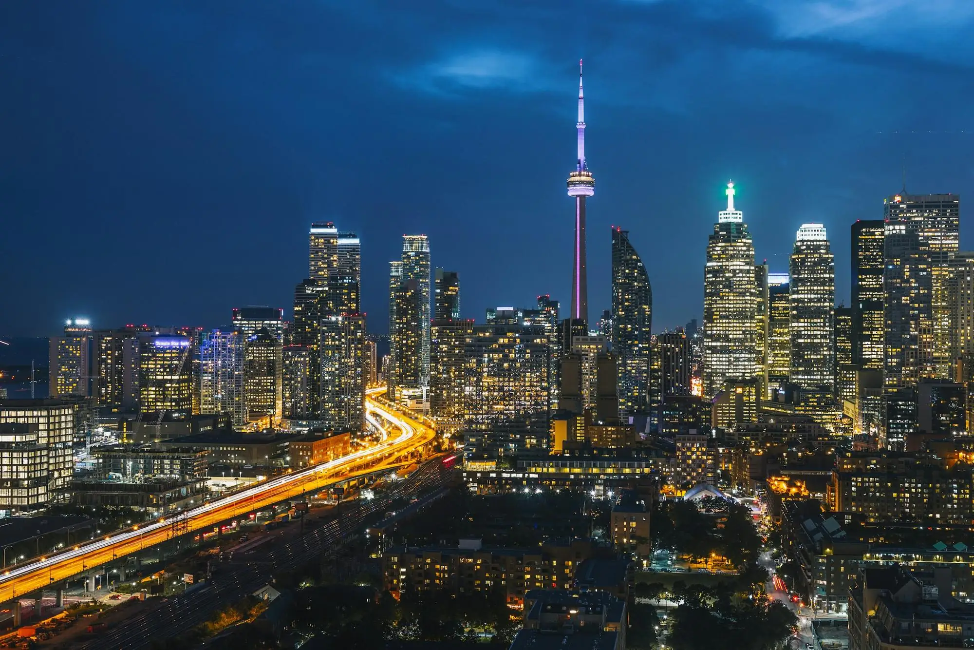 Toronto at night: the CN Tower above the downtown skyline, with streaks of traffic light along the expressway